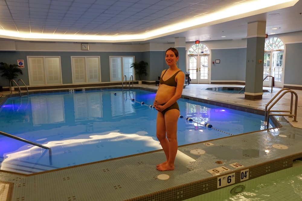 Audrey enjoying the saline pool at Fairmont Hotel Macdonald Audrey Bergner of That Backpacker, very pregnant with baby Aurelia, stands at the edge of the Fairmont Hotel Macdonald’s indoor saline pool, enjoying a quiet babymoon moment surrounded by warm lighting, calm blue water and the hotel’s elegant heritage-style spa space.