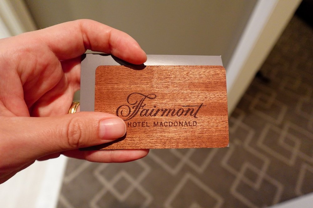 Fairmont Hotel Macdonald wooden room key card A close-up of a Fairmont Hotel Macdonald room key card shows its distinctive wood-grain design and engraved logo, held in hand against the patterned carpet of the Edmonton heritage hotel, capturing the tactile, elegant details that set the property’s Fairmont Gold experience apart.