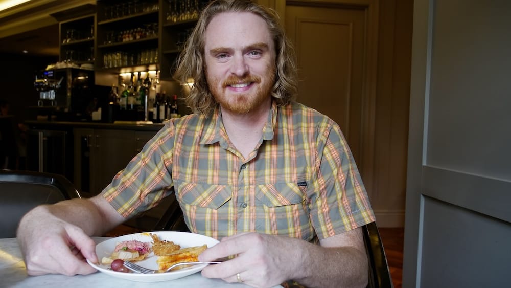 Samuel Jeffery enjoying canapés in the Fairmont Gold Lounge at Fairmont Hotel Macdonald in Edmonton, Alberta Samuel Jeffery sits with a plate of canapés in the Fairmont Gold Lounge at Fairmont Hotel Macdonald in Edmonton, Alberta, Canada, with the lounge bar visible behind him.