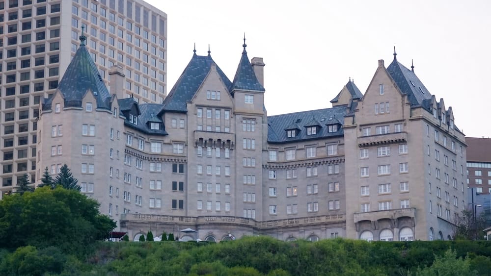 Vista exterior del Fairmont Hotel Macdonald, un hotel histórico de estilo château con techos de torretas verdes, visto desde el valle del río en el centro de Edmonton, Alberta.