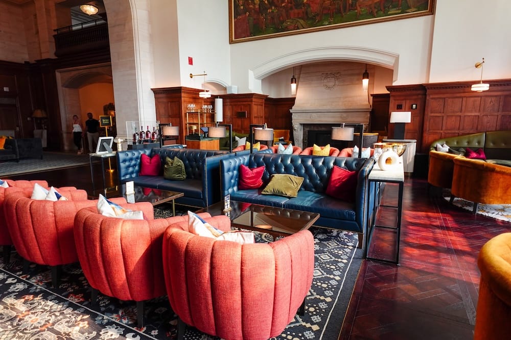 El lobby del Fairmont Hotel Macdonald en Edmonton, Alberta, Canadá, con paneles de madera oscura, sillones tapizados de colores, alfombras estampadas y una gran chimenea.