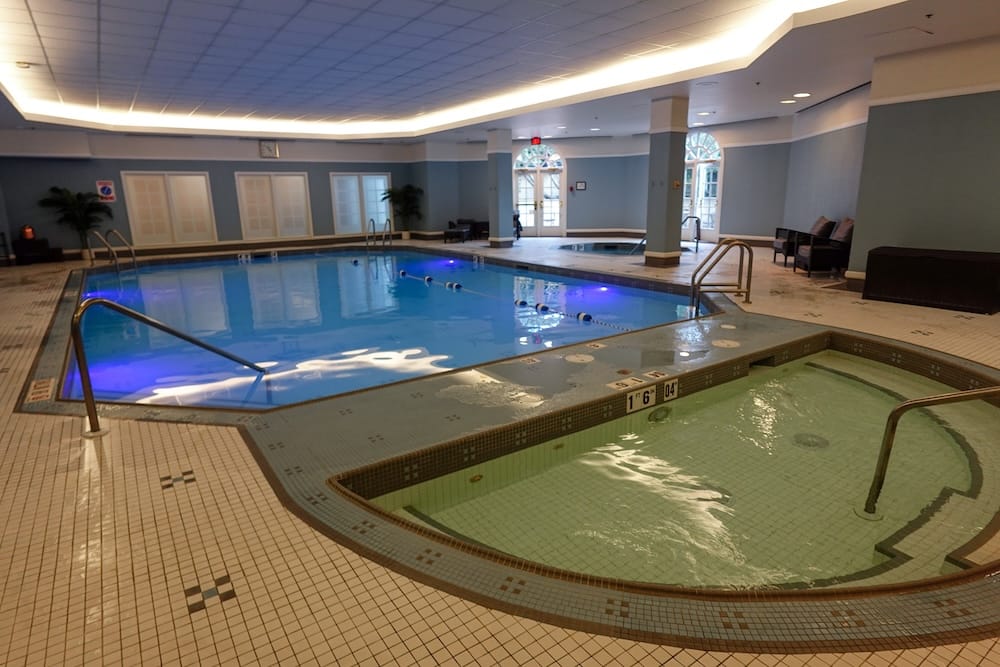 Piscina salina e hidromasaje del Fairmont Hotel Macdonald en Edmonton, Alberta, Canadá Instalaciones de piscina cubierta del Fairmont Hotel Macdonald en Edmonton, Alberta, Canadá, con piscina rectangular de agua salina, hidromasaje contiguo, piso de baldosas, pasamanos y asientos.
