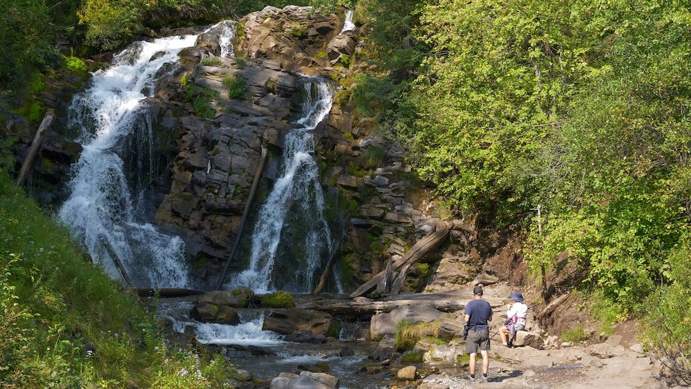 Fairy Creek Falls hike near Fernie Hikers pause near the base of Fairy Creek Falls outside Fernie, British Columbia, where water cascades over layered rock into a shaded forest setting, showing how easily visitors can step from town history into alpine nature.