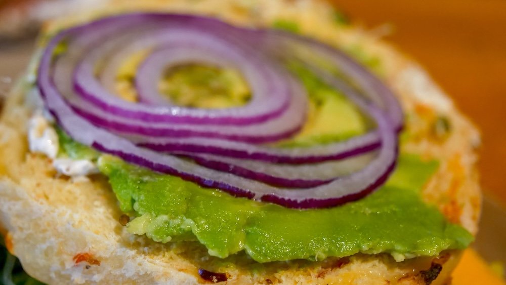 Avo Launcher bagel at Big Bang Bagels in Fernie Fernie, British Columbia breakfast close-up at Big Bang Bagels showing the Avo Launcher bagel topped with creamy avocado, red onion, and spread, highlighting a filling, family-friendly breakfast stop before exploring Fernie with a baby.