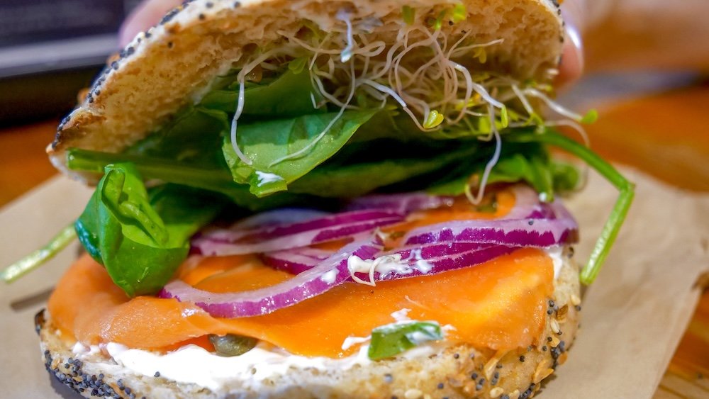 Fernie, BC Big Bang Bagels Switchback Salmon bagel Fernie, BC close-up of the Switchback Salmon bagel from Big Bang Bagels, showing smoked salmon, cream cheese, red onion, fresh greens, and sprouts layered on a toasted everything bagel—one of Fernie’s most popular and satisfying breakfast options.