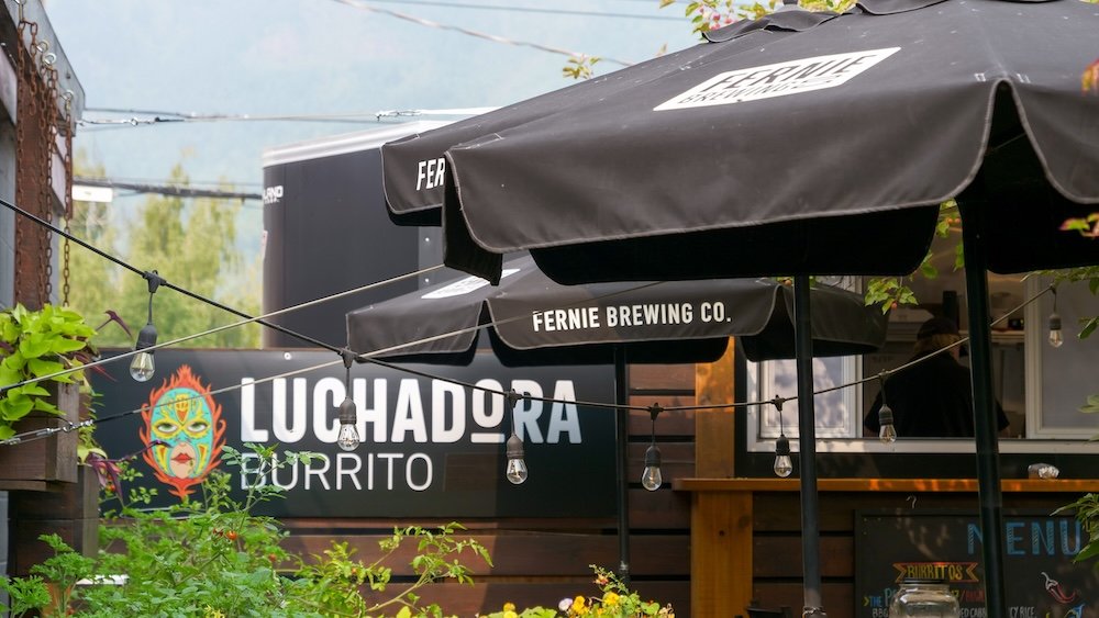 Luchadora Burrito Co patio sign in downtown Fernie, BC Fernie, British Columbia, Luchadora Burrito Co patio sign framed by greenery and umbrellas downtown, highlighting a popular casual eatery known for hearty burritos and quick meals that fuel hiking, biking, and sightseeing around town.