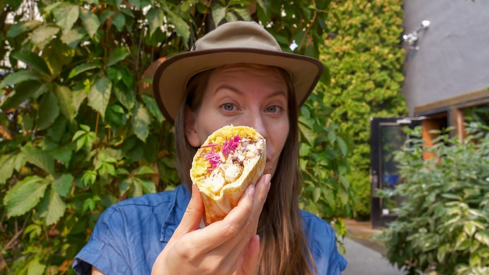 Fernie, British Columbia patio at Luchadoro Burrito Co as Audrey Bergner holds the Fishy Boy burrito, highlighting a popular downtown Fernie food stop and the fresh, flavourful seafood filling enjoyed during a casual mountain-town meal.