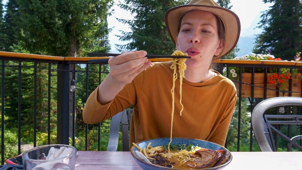 Fernie, British Columbia post-hike dining scene as Audrey Bergner enjoys a bowl of miso ramen at Bear Bistro at Island Lake Lodge, savoring a warming, comforting meal with forest and mountain views after hiking nearby Fernie trails.
