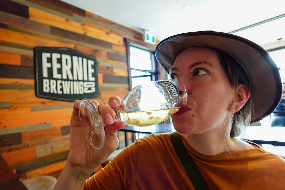 Non-alcoholic beer options at Fernie Brewing Company Audrey Bergner of That Backpacker enjoying a non-alcoholic beer inside Fernie Brewing Company in Fernie, British Columbia, showing that the tasting room offers inclusive options for designated drivers, parents, and travellers who want the brewery experience without alcohol.