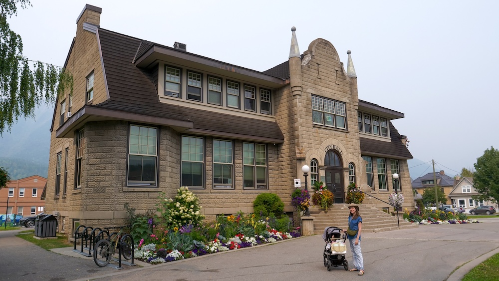 Fernie City Hall gardens after visiting Fernie Museum Audrey Bergner of That Backpacker stands with baby Aurelia in a stroller outside Fernie City Hall after visiting the Fernie Museum, admiring the historic stone architecture and colorful flower gardens that make this downtown stop a relaxing pause on the Fernie Heritage Walk.