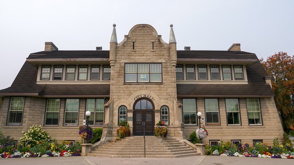 Historic Fernie City Hall downtown Fernie City Hall in downtown Fernie, British Columbia, photographed on an overcast day, showing the historic stone façade, symmetrical windows, and colorful seasonal flower beds that make this civic building a key stop on the Fernie Heritage Walk.