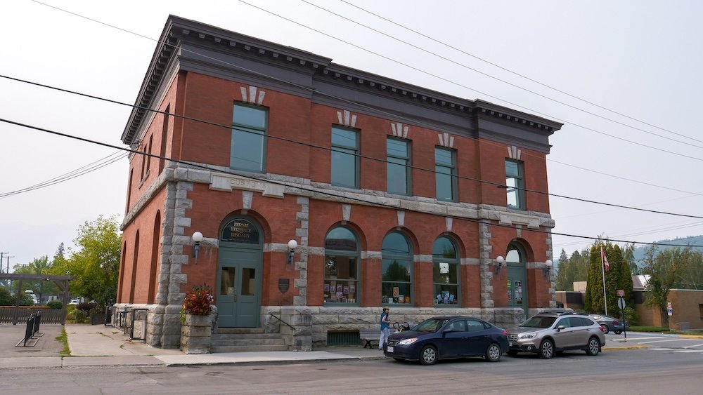 Fernie Heritage Library, originally built as the Post Office and Customs Office in 1907, stands on 3rd Avenue with arched windows, stone detailing, and red brick walls, surviving the Great Fire and anchoring Fernie’s self-guided heritage walking tour.
