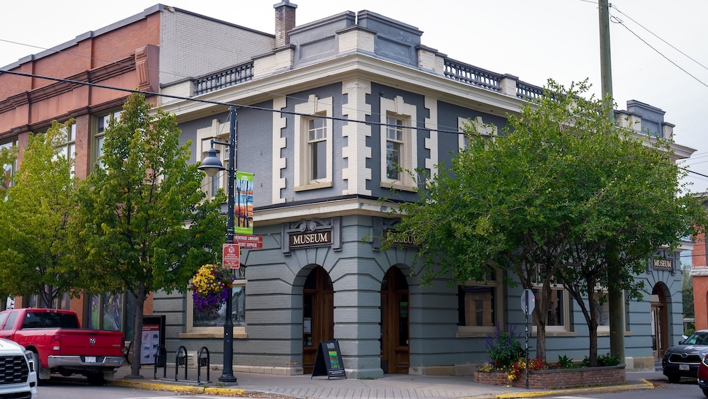 Fernie Museum historic building exterior Exterior of the Fernie Museum in downtown Fernie, British Columbia, housed in the former Home Bank building with arched entrances and ‘Museum’ signs. A classic street-corner view with trees, planters, and heritage brick neighbours.