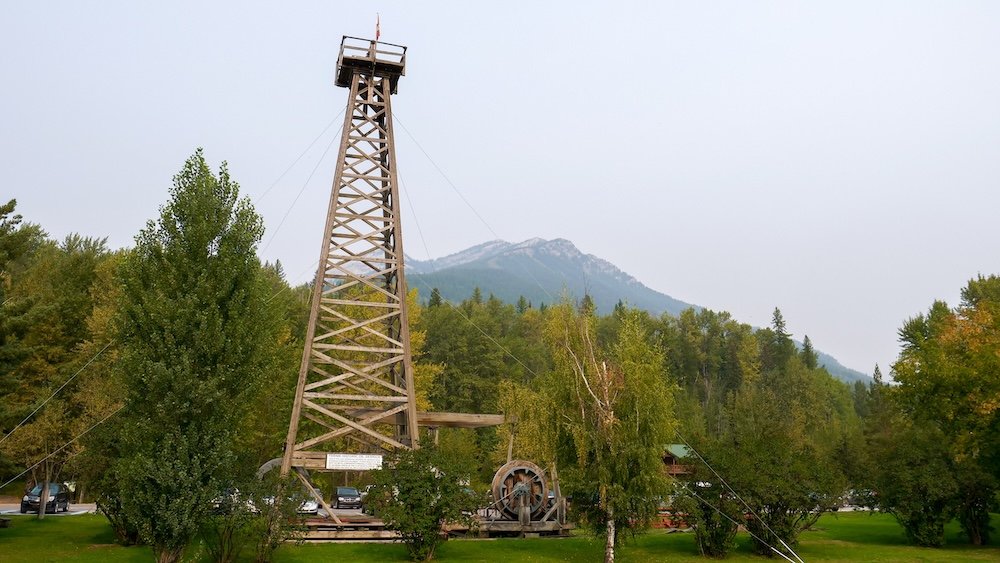 The Fernie Oil Derrick beside the Fernie Visitor Information Centre in Fernie, British Columbia, highlighting an important historic landmark connected to the region’s industrial past, with green parkland and mountain scenery that travelers often explore during a two-day Fernie itinerary.
