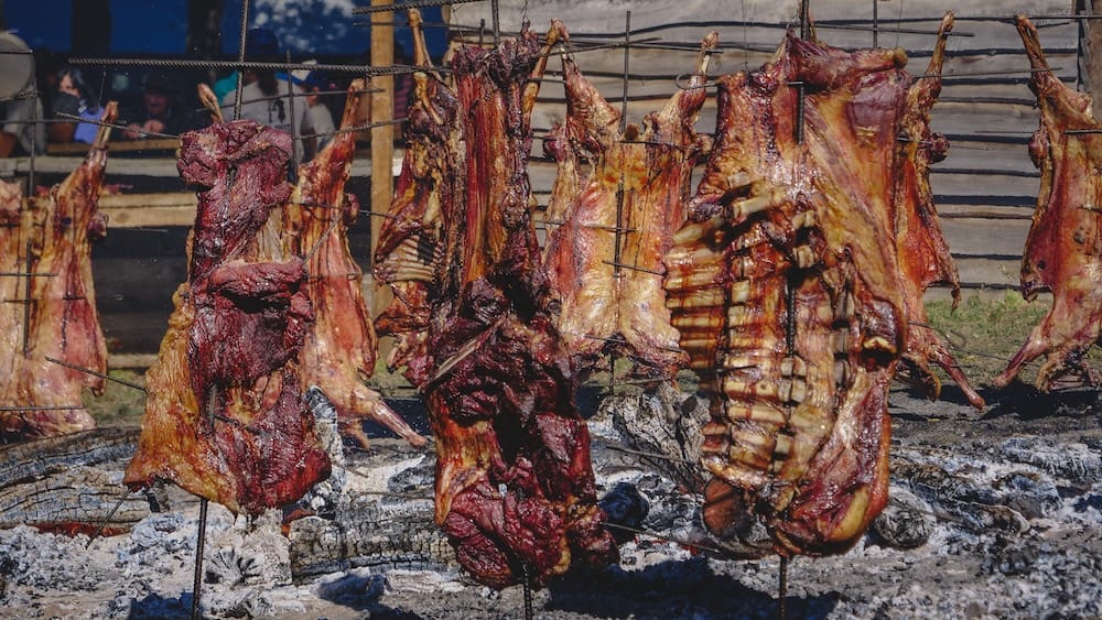 Cordero asado al asador Cholila Patagonia gaucho cooking Fiesta Nacional del Asado Cholila Patagonia whole lambs roasting on iron crosses over open embers, showing traditional asado al asador cooking where gauchos slowly prepare cordero using fire, patience, and technique.
