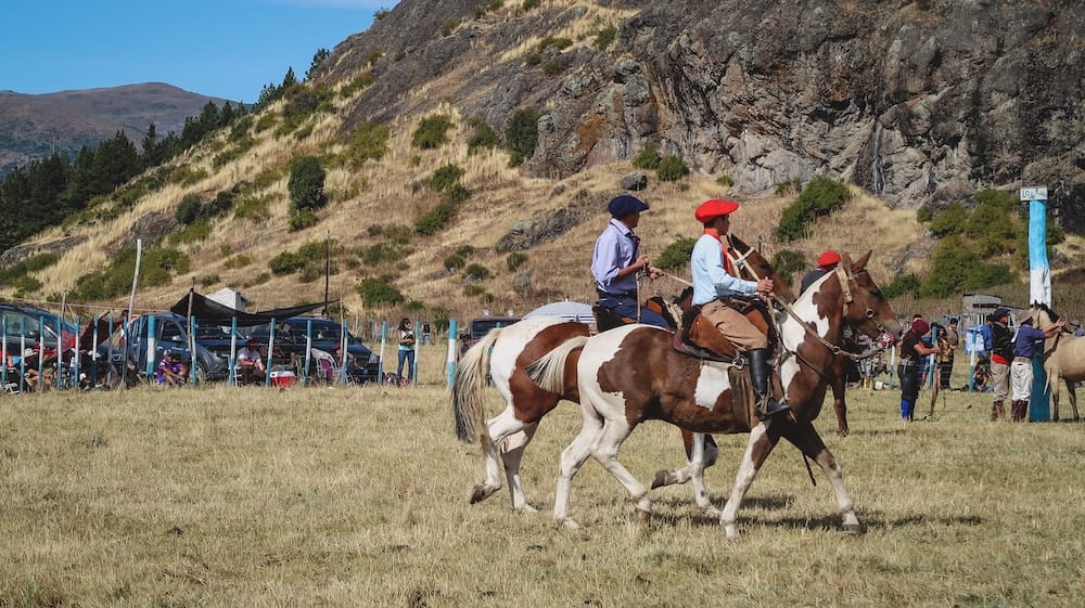 Gauchos riding horses Cholila Patagonia rural festival Fiesta Nacional del Asado Cholila Patagonia gauchos riding horses across an open field during a rural gathering, showing traditional horsemanship and community participation where riding remains a core part of everyday gaucho life.