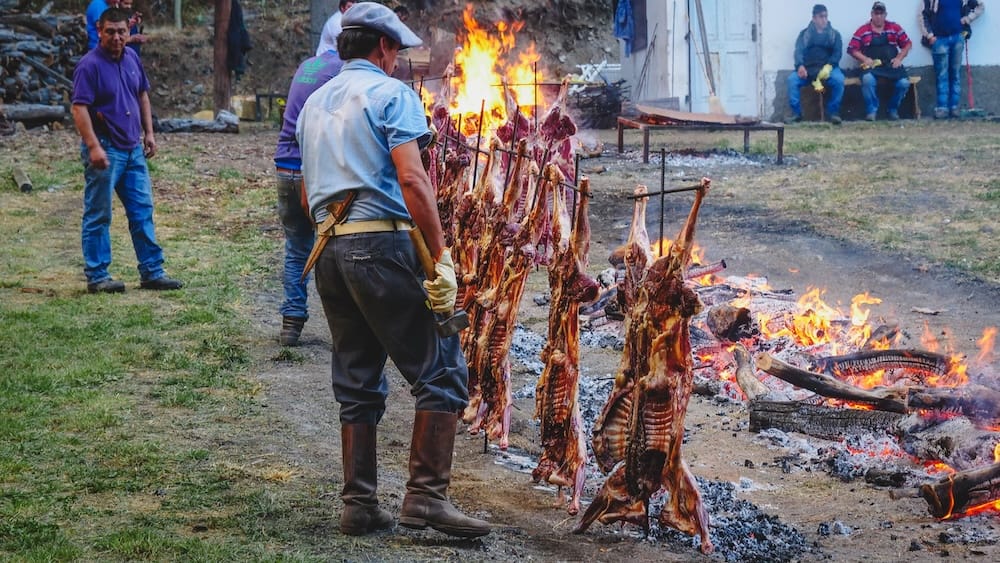 Gauchos roasting Patagonian lamb on iron crosses over open fire at Fiesta Nacional del Asado in Argentina, showcasing traditional cordero al asador method, outdoor cooking, multiple carcasses, and authentic gaucho grilling techniques in Patagonia
