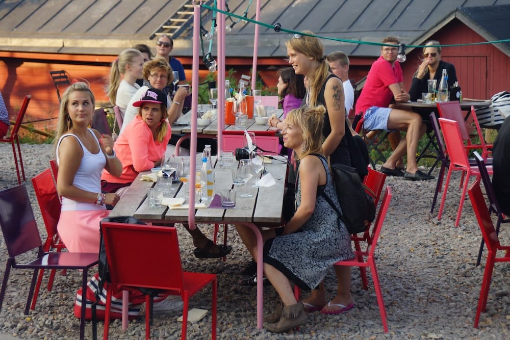 People eating and drinking at a lively outdoor terrace in Helsinki during summer, with colourful chairs, shared tables and relaxed social dining that reflects Finland’s long-light seasonal atmosphere.
