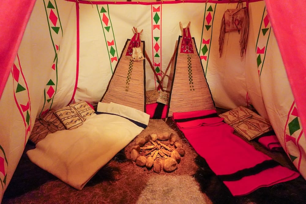 First Nations display inside the Royal Alberta Museum in Edmonton, Alberta, Canada, showing a painted tipi interior with bedding, woven backrests, decorated bags and a central stone hearth.