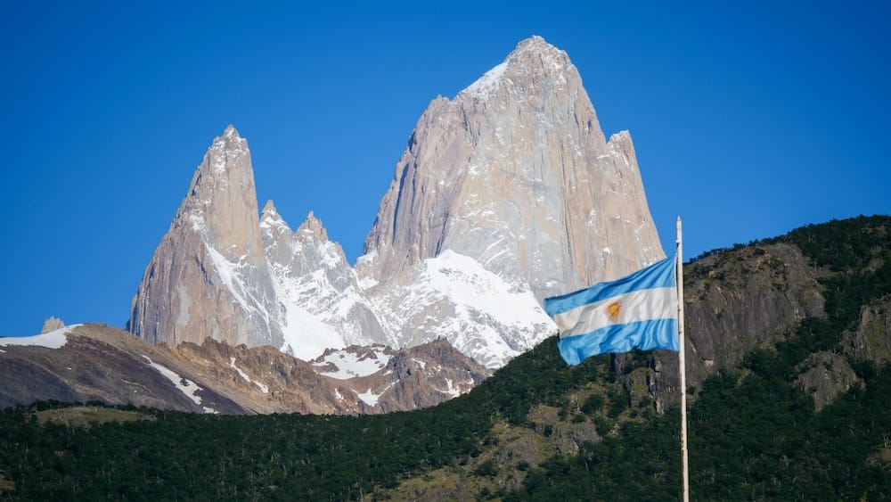 Mount Fitz Roy towering above El Chalten in Patagonia Argentina with the Argentine flag in the foreground, capturing the region’s iconic Andes landscape and national identity.
