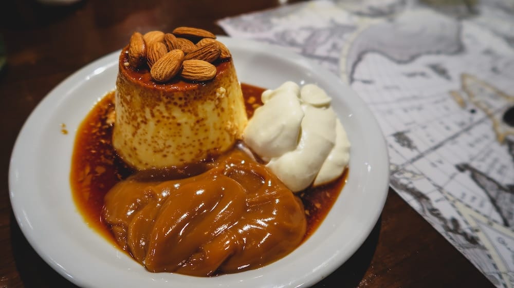 Flan with dulce de leche in El Bolsón topped with almonds and served with whipped cream and an oversized portion of caramel, a classic Argentine dessert that highlights Patagonia’s generous servings and rich sweet flavors
