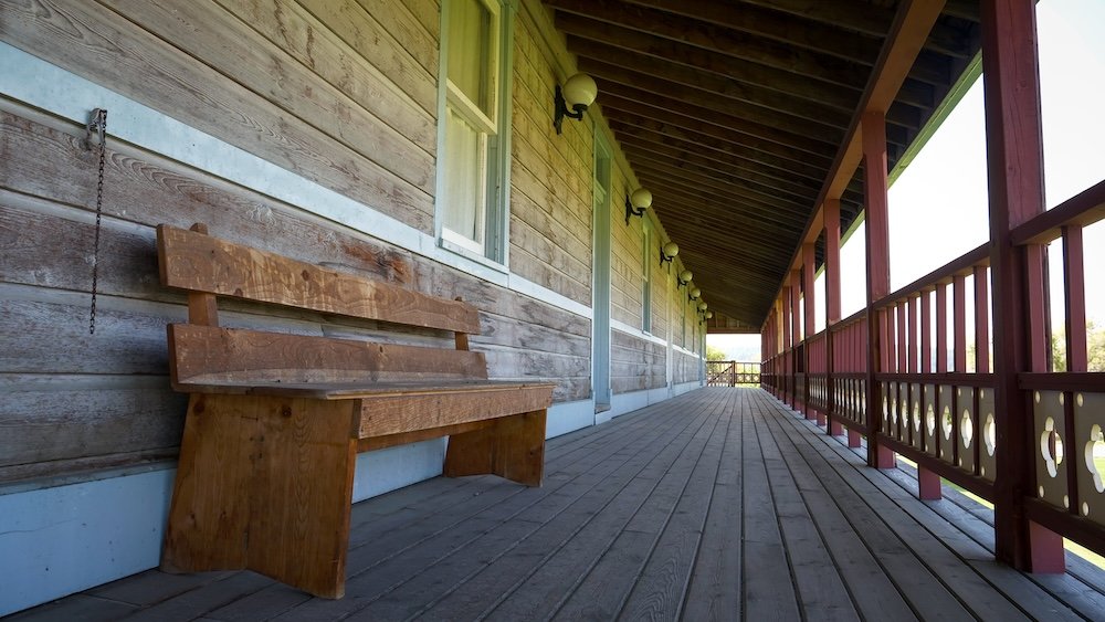 Bench on the covered wooden boardwalk at Fort Steele Heritage Town near Cranbrook, BC, showing simple frontier seating along a historic building porch, with weathered planks, railing details, and long shaded walkways typical of a preserved 1890s town.
