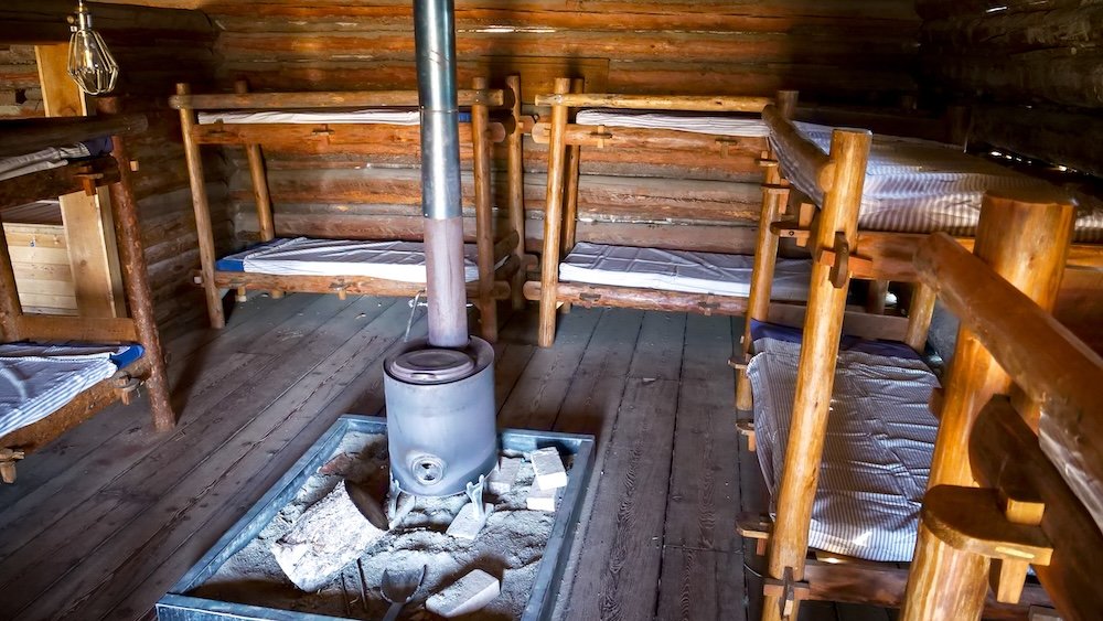 Interior of a historic bunkhouse at Fort Steele Heritage Town near Cranbrook, BC, showing wooden bunk beds arranged around a central wood-burning stove, offering a realistic glimpse into how workers and residents lived during the town’s frontier era.