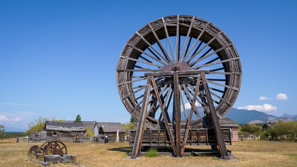 Fort Steele Heritage Town near Cranbrook, BC, featuring a large wooden wheel structure rising above historic buildings and open grassland, highlighting the site’s distinctive frontier-era engineering and unusual architecture visitors encounter while exploring the town.
