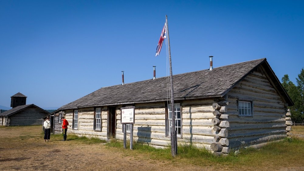 Fort Steele Heritage Town near Cranbrook, BC, showing the historic Steele Cabin built from hand-hewn logs beneath a clear blue sky, helping visitors understand early settlement life and the modest living conditions tied to the site’s NWMP-era history.
