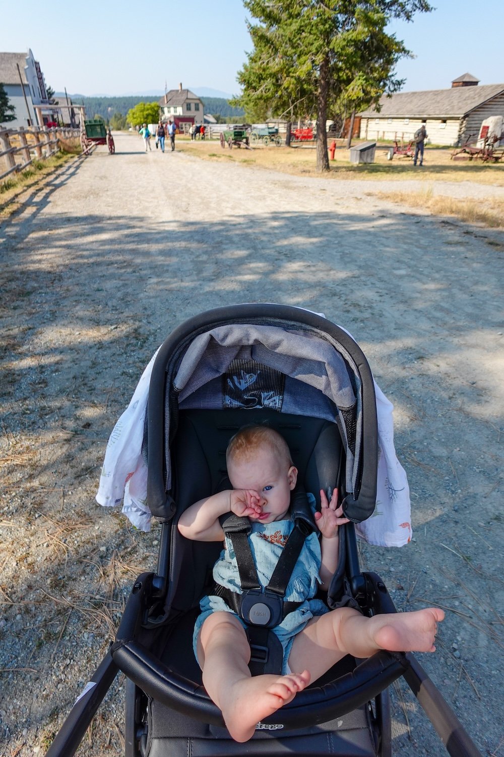 Fort Steele Heritage Town near Cranbrook, BC, as baby Aurelia relaxes in a stroller while being pushed along the wide gravel streets, showing the open layout, gentle pacing, and stroller-friendly paths that make this living history town work well for families.