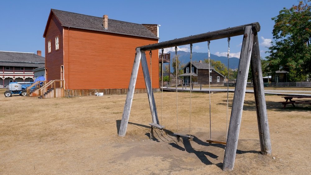 Playground-style wooden swings for kids and toddlers at Fort Steele Heritage Town near Cranbrook, BC, set beside historic buildings and open lawns, showing how this living history site includes simple play areas that help families take relaxed breaks.