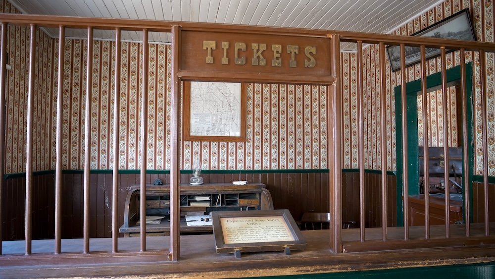 Historic ticket counter inside a heritage building at Fort Steele Heritage Town near Cranbrook, BC, featuring the original “Tickets” sign, wooden bars, and period decor that show how visitors once purchased admission and services in the town’s early days.
