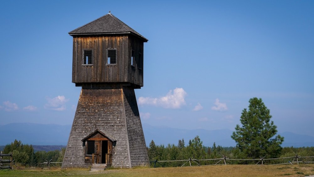 A distinctive wooden tower-style building at Fort Steele Heritage Town near Cranbrook, BC, standing alone against open fields and distant Kootenay mountains, highlighting the unusual architecture and frontier-era structures visitors can explore on site.