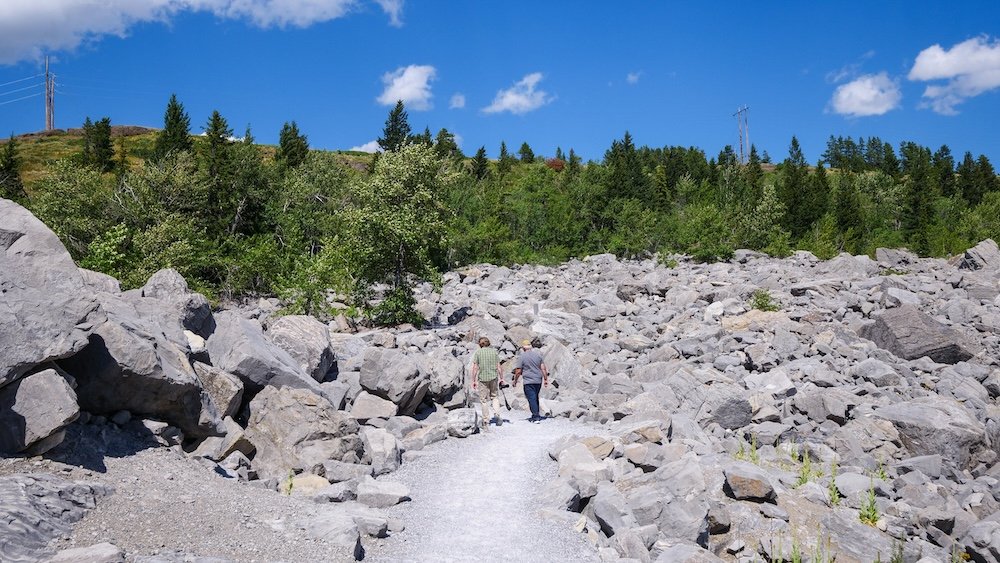 Hikers walking the Frank Slide Interpretive Trail in Crowsnest Pass, Alberta, surrounded by massive limestone boulders from the 1903 slide, making this an easy and educational roadside stop on the drive from Calgary to Fernie.
