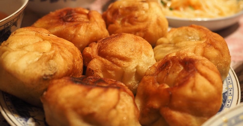 Close-up of golden fried stuffed pastries with pleated tops served on a shared plate during a family meal in Karakol, Kyrgyzstan, alongside other dishes from the generous Central Asian table.
