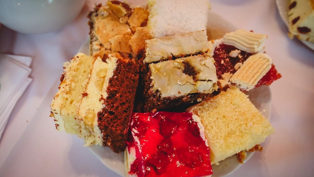 An assortment of colorful Welsh cakes and desserts served during merienda in Gaiman, Argentina, featuring sponge cakes, jam-filled slices, and layered pastries that showcase the variety and abundance of Patagonia’s tea house tradition.
