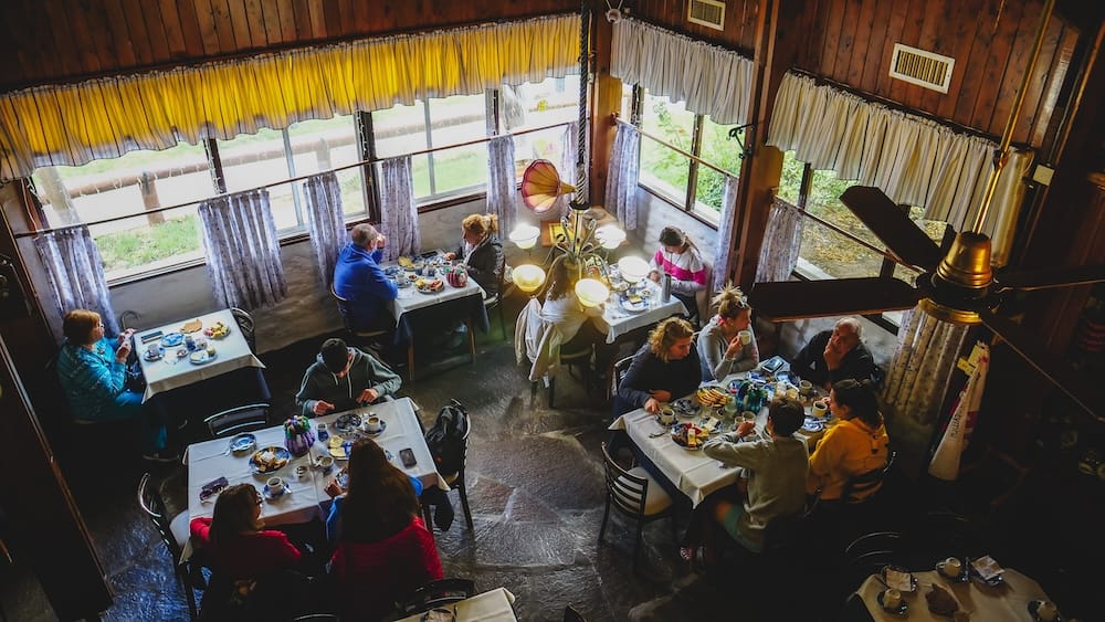 A busy Welsh tea house scene at Ty Gwyn in Gaiman, Argentina, with multiple tables enjoying a traditional Patagonian merienda of tea, cakes, and pastries, illustrating the communal and immersive nature of this afternoon tea tradition.
