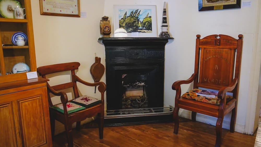Welsh heritage display with carved wooden chairs, fireplace, and cultural artifacts inside the Museo Histórico Regional in Gaiman, Patagonia, illustrating how Y Wladfa settlers recreated elements of Welsh domestic life in a remote and challenging environment.
