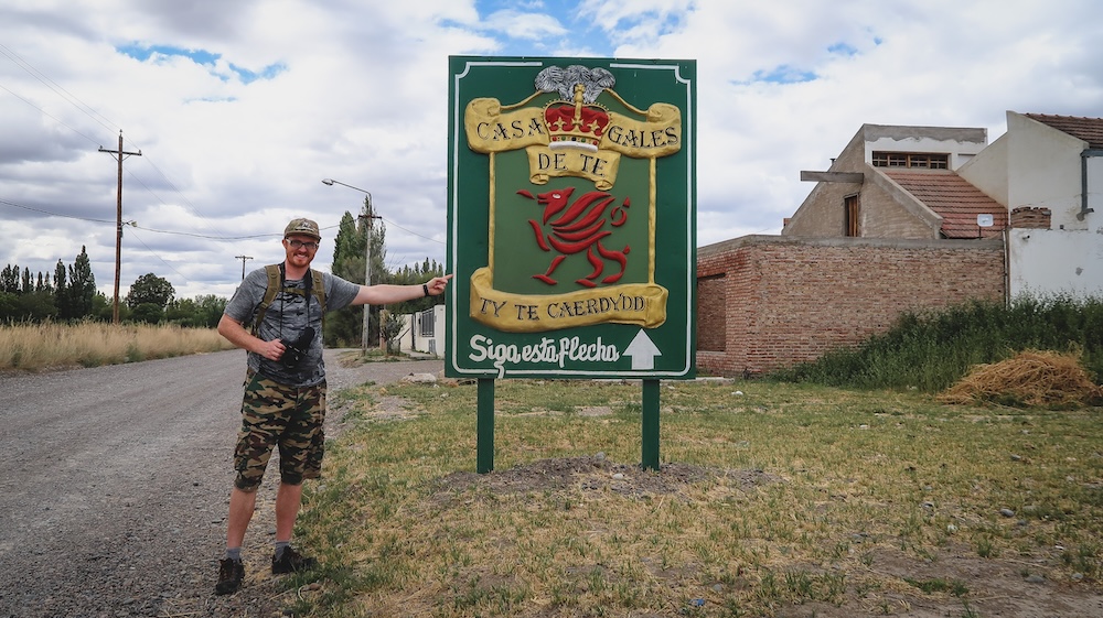 Samuel Jeffery beside Welsh tea house sign in Gaiman Patagonia Argentina Gaiman Welsh tea house sign in Chubut Patagonia Argentina where Samuel Jeffery stands beside the Casa Gales de Té sign highlighting the Welsh colony heritage that shaped towns across the Patagonian steppe after the 1865 migration.