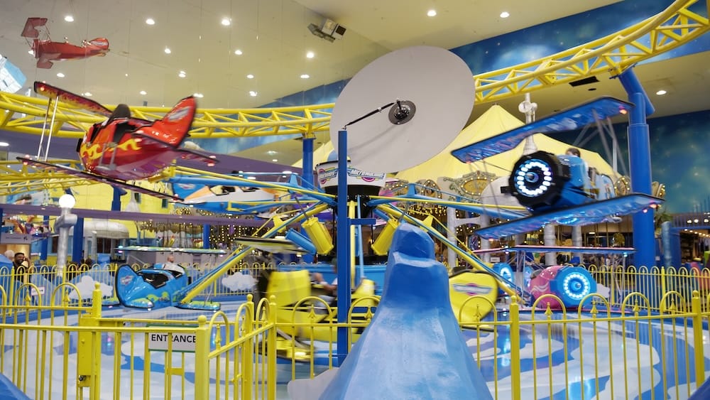 Galaxyland Airplane Ride at West Edmonton Mall in Edmonton, Alberta Colourful airplane ride vehicles spinning beneath yellow tracks inside Galaxyland at West Edmonton Mall in Edmonton, Alberta, with families riding under bright indoor lights.