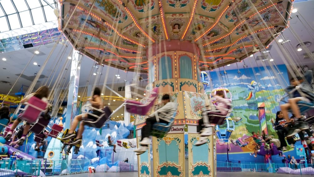 Galaxyland Indoor Swing Ride at West Edmonton Mall in Edmonton, Alberta, Canada Riders swing through a brightly lit attraction inside Galaxyland at West Edmonton Mall in Edmonton, Alberta, Canada, with colourful murals, motion blur and other indoor amusement rides visible in the background.