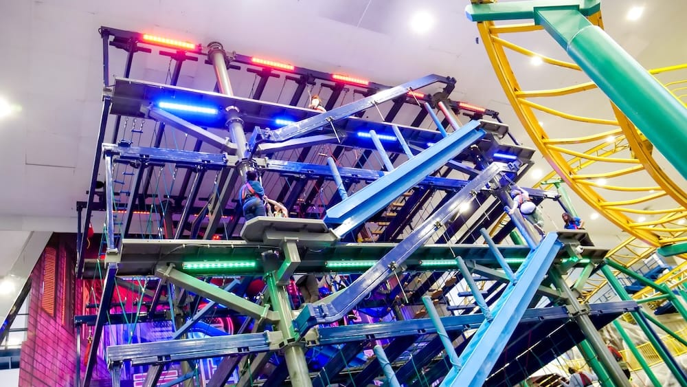 Indoor amusement ride at Galaxyland inside West Edmonton Mall in Edmonton, Alberta, Canada, with riders seated on a large multilevel mechanical attraction beneath colourful lights and roller-coaster track.