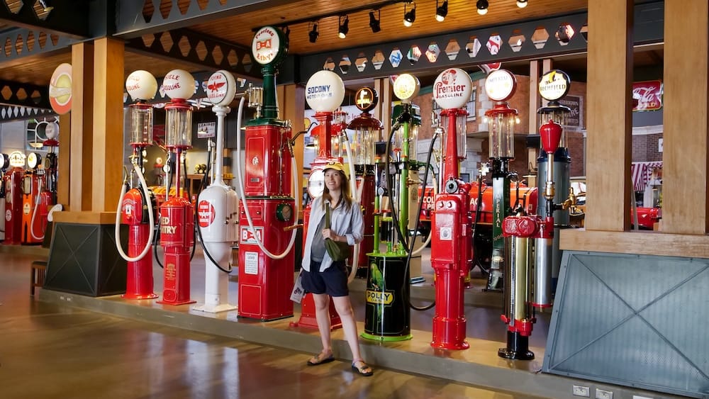 Audrey Bergner standing among colorful vintage gasoline pumps inside Gasoline Alley Museum at Heritage Park in Calgary, Alberta, Canada.