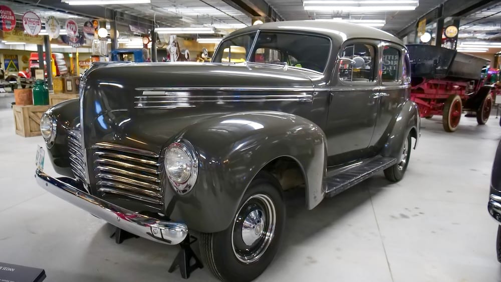 Restored gray vintage sedan displayed inside Gasoline Alley Museum at Heritage Park in Calgary, Alberta, Canada, with historic vehicles, gasoline signs and museum displays visible behind it.