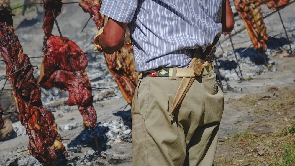 Cordero al palo Fiesta Nacional del Asado Cholila, primer plano de gaucho con facón tradicional asando en Patagonia Argentina