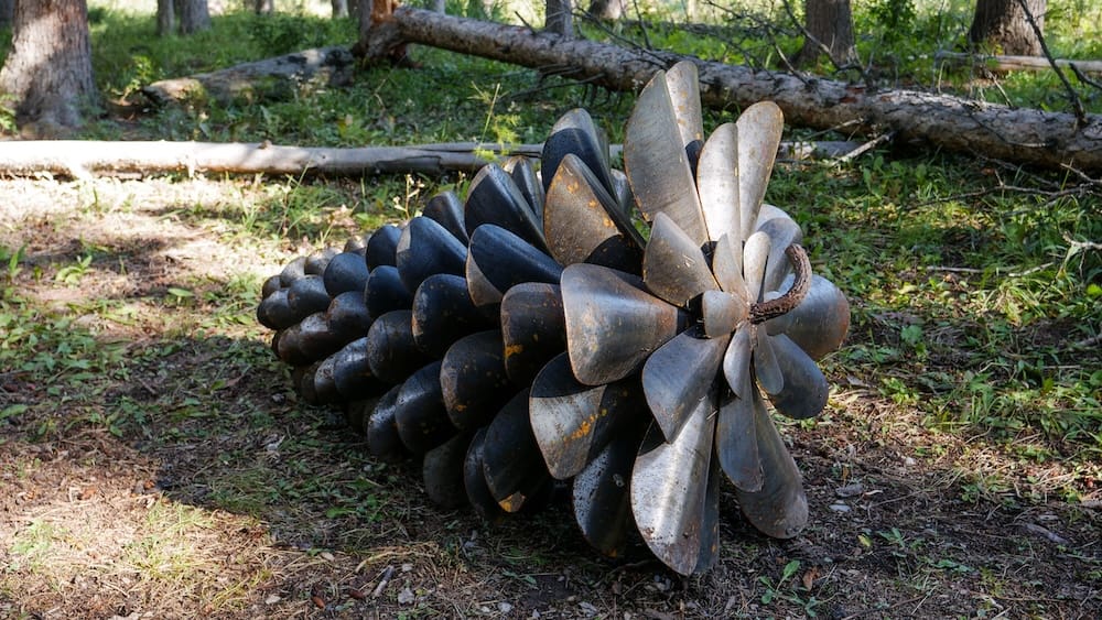Metal pinecone sculpture on the Art in Nature Trail, Banff, Alberta, Canada A giant sculpture shaped like a pinecone, made from rusted metal petals, rests on the forest floor along the Art in Nature Trail in Banff, Alberta, Canada.