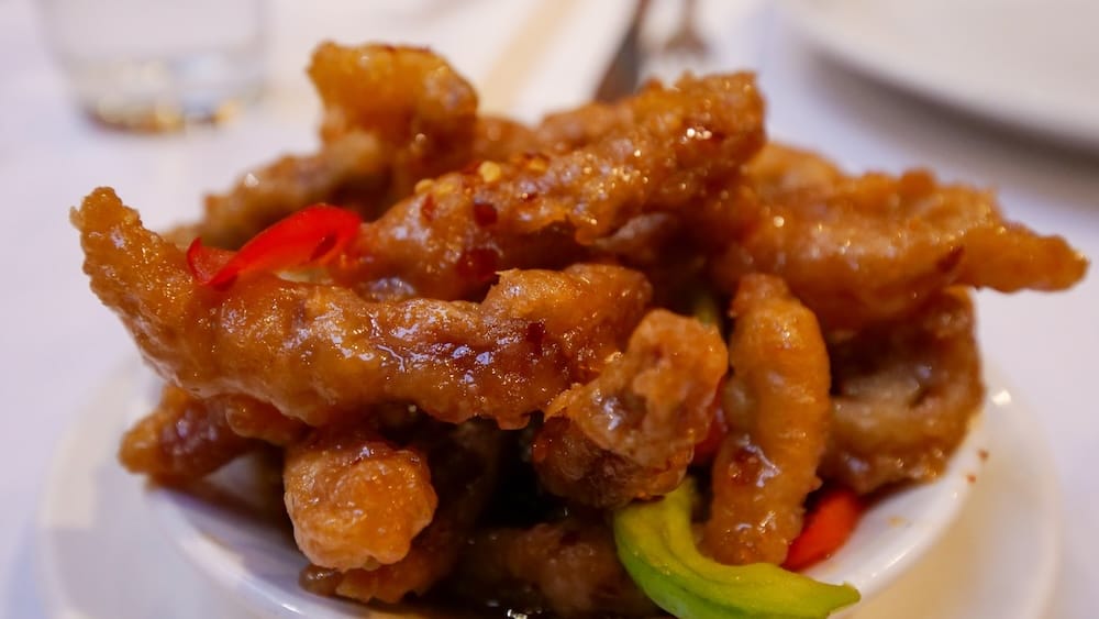 Close-up of ginger beef in Calgary Chinatown, Alberta, Canada, showing crispy strips of fried beef coated in a glossy sweet sauce with red pepper and green vegetables.