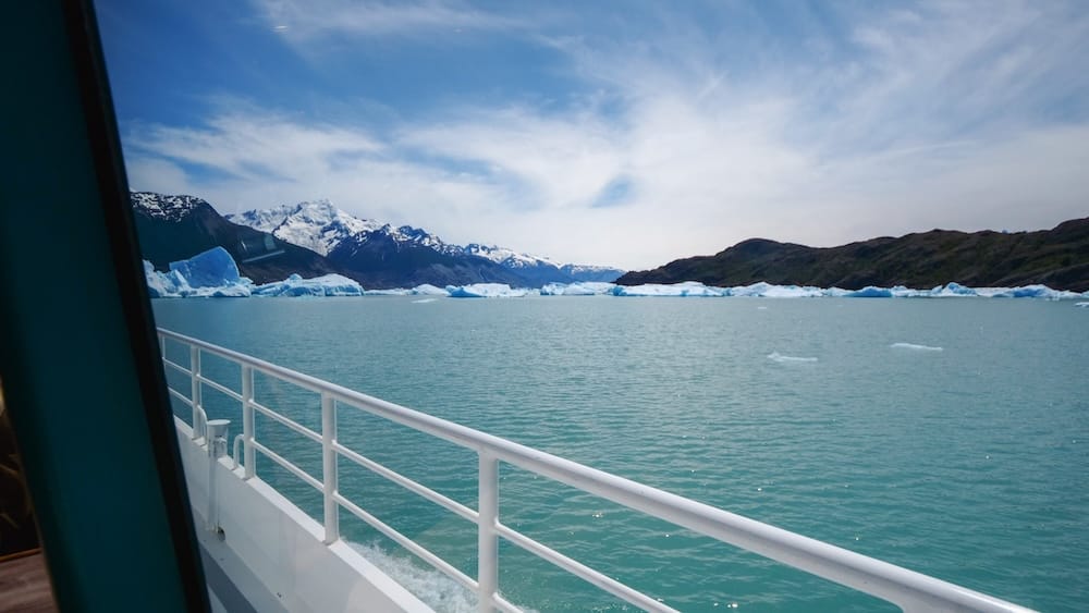 Icebergs drifting near Perito Moreno Glacier on Lago Argentino in Patagonia, Argentina Blue-white icebergs drift across Lago Argentino near Perito Moreno Glacier in Santa Cruz, Patagonia, Argentina, viewed from the side of a glacier tour boat beneath distant snowcapped mountains.