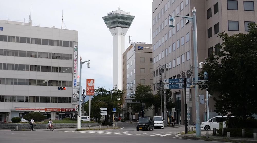 Calle del barrio de Goryokaku en Hakodate, Hokkaido, Japón, con la Torre Goryokaku al fondo Escena urbana en la zona de Goryokaku, Hakodate, Hokkaido, Japón, con edificios de oficinas, ciclistas y la Torre Goryokaku elevándose al fondo sobre este barrio bien conectado por tranvía.