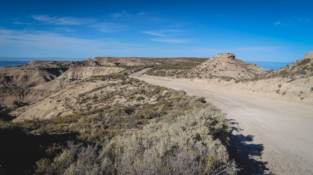 Gravel road across the arid steppe near Puerto Pirámides, Peninsula Valdés, Chubut, Patagonia, Argentina A winding gravel road cuts through dry scrubland and steppe cliffs above the coastline near Puerto Pirámides on Peninsula Valdés, Chubut, Patagonia, Argentina, with the ocean visible in the distance.